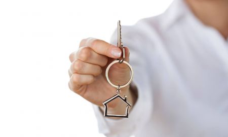 Person in weißem Kittel reicht einen Schlüssel mit Hausschlüsselanhänger.