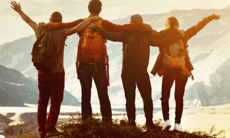 Vier Personen wandern Arm in Arm in der Natur mit Aussicht auf Bergen im Hintergrund