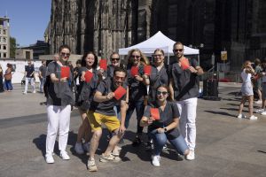 Gruppenbild von Personen, die schwarze Oberteile tragen und ein rotes Papier in die Luft halten