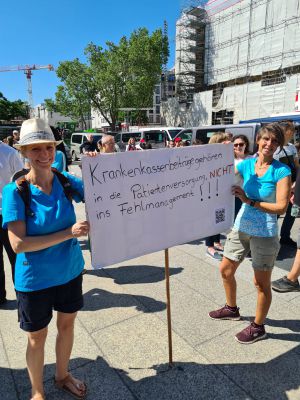 Zwei Personen mit einem Schild in der Hand stehen lächelnd bei einem Protest in Köln